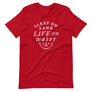 Red unisex t-shirt with wording in white, "Sleep on Land, Live on Water" written in black artistic lettering on front. Underneath this is very small semi circle stating "Mutineer Bay" centered with small anchor. All lettering and images are in white.